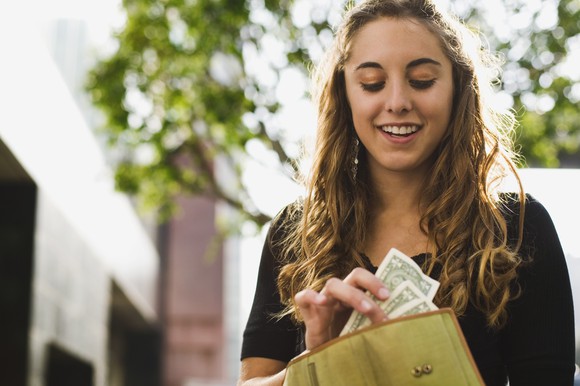 Smiling person withdrawing several bills from a wallet.