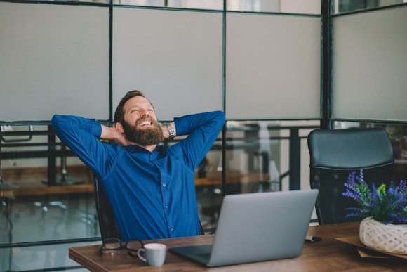 A man smiles while working on a laptop.