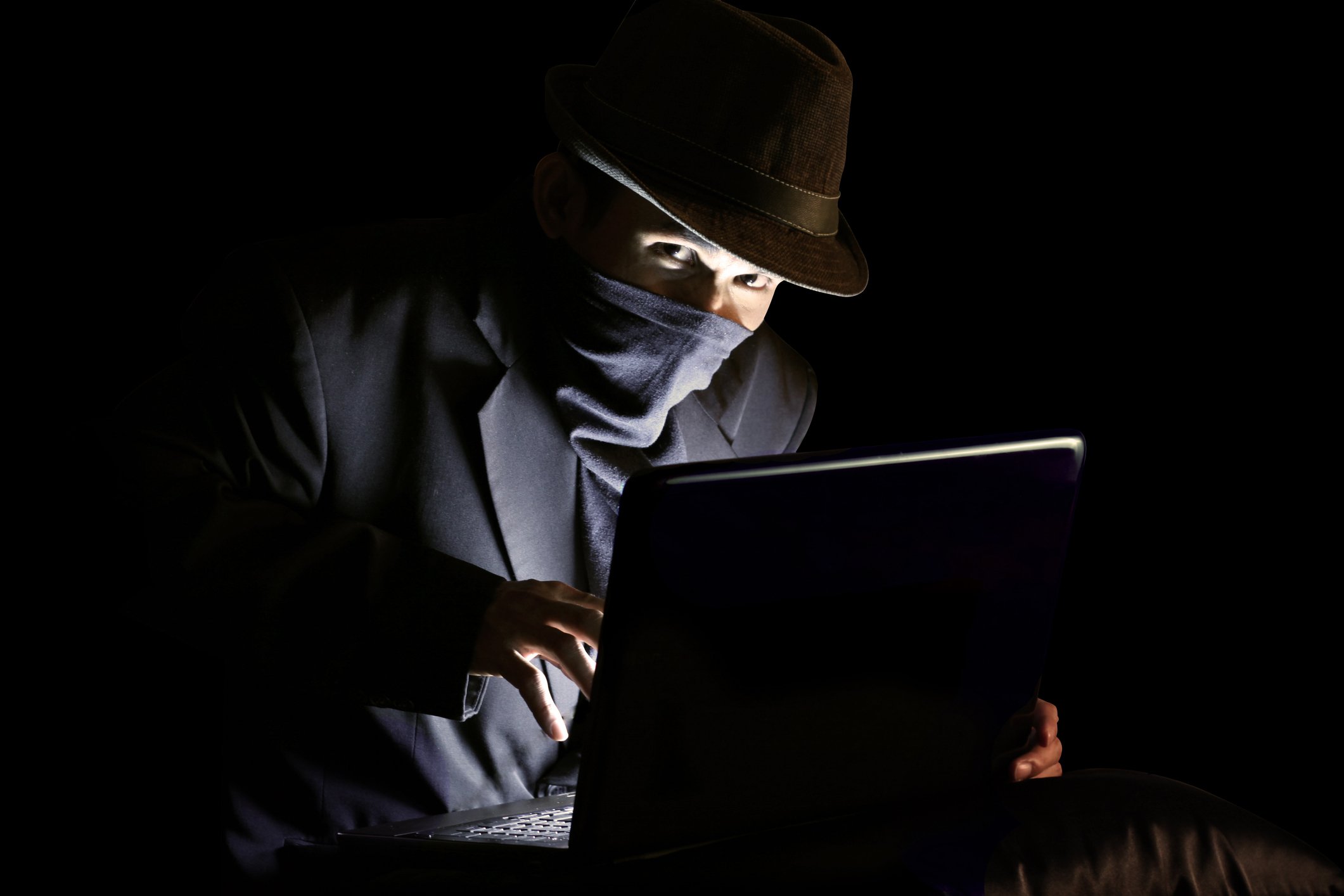 A hacker using a laptop in a dimly lit room.