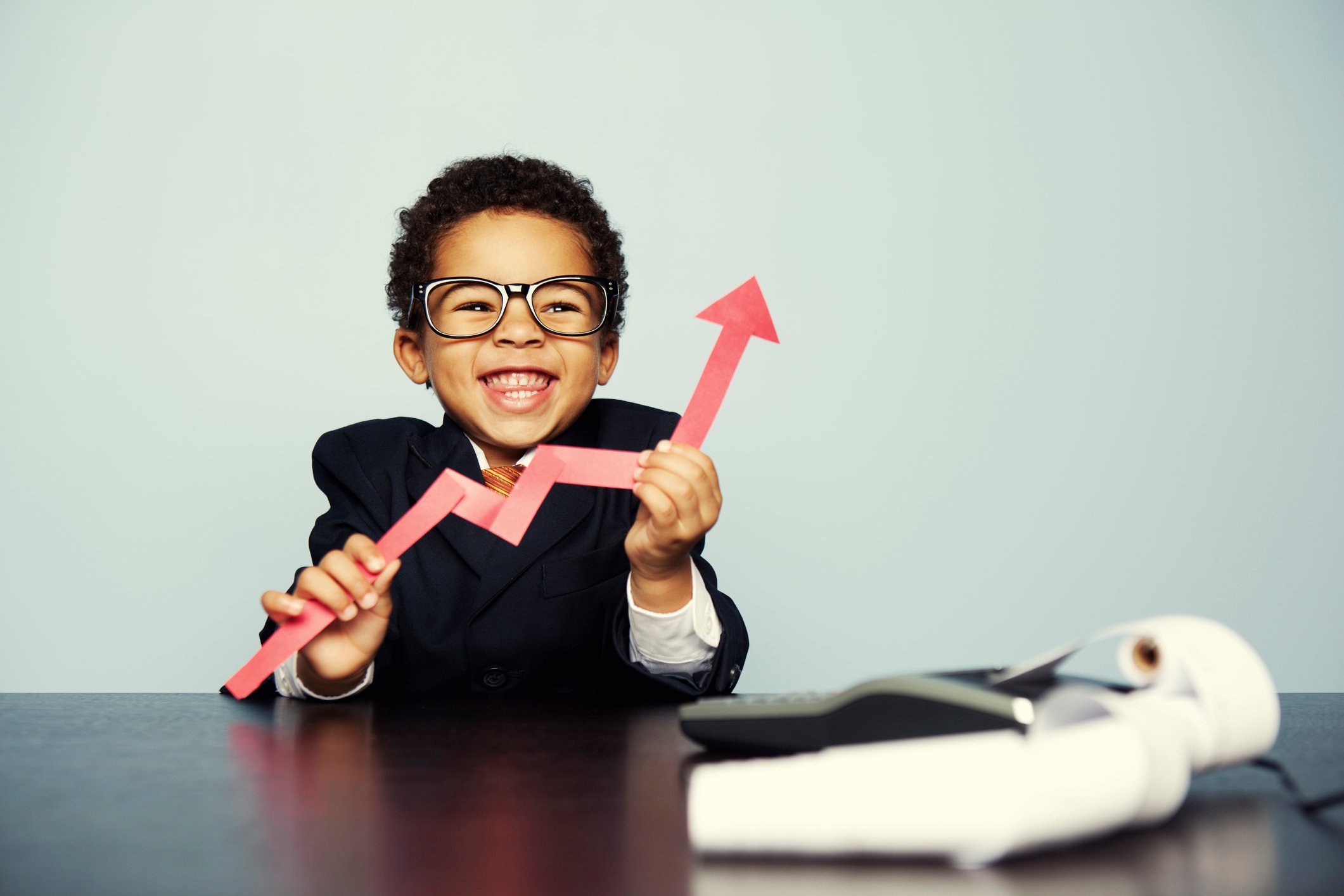 A child in a business suit holds a cutout of a rising chart.