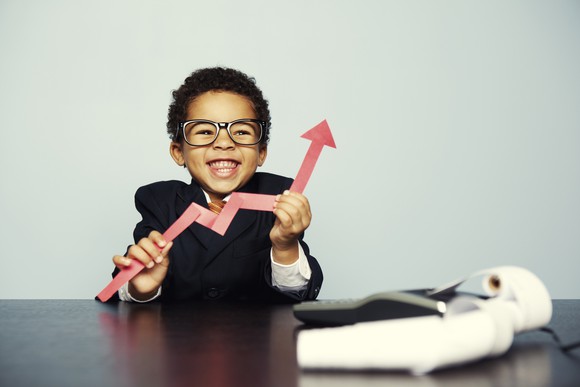 A child in a business suit holds a cutout of a rising chart.