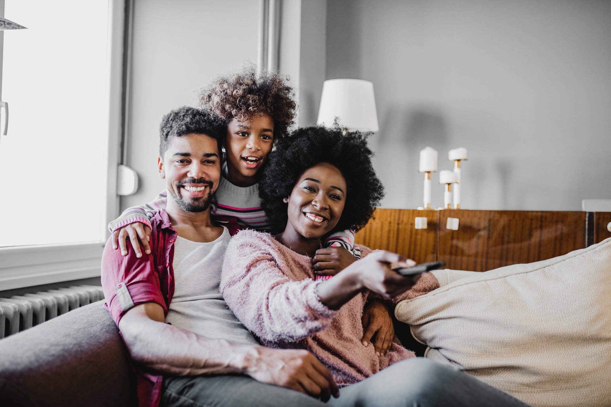 A man, woman, and child sitting on a couch, the woman holding a remote control.