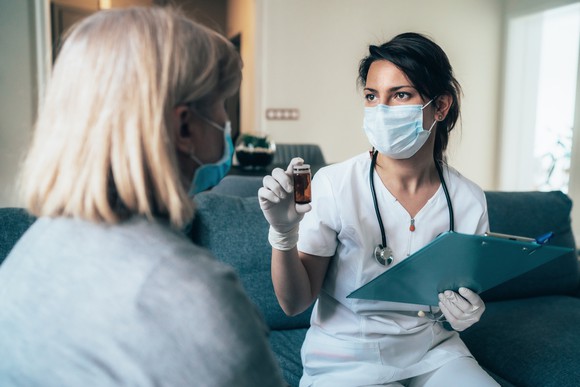 A doctor shows a bottle of antiviral pills to a patient while sitting in a clinic room.