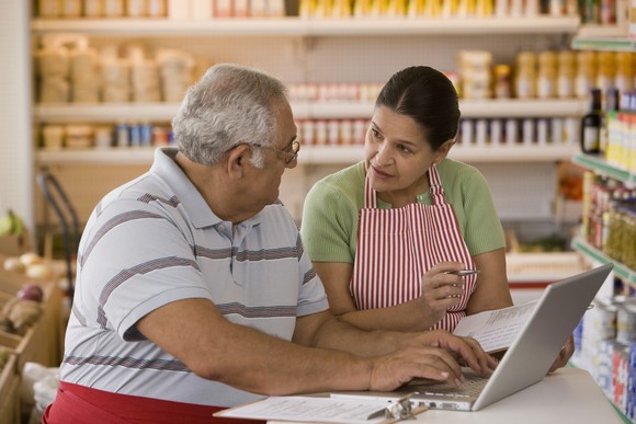 Two people in a small store discuss businss while using a laptop.