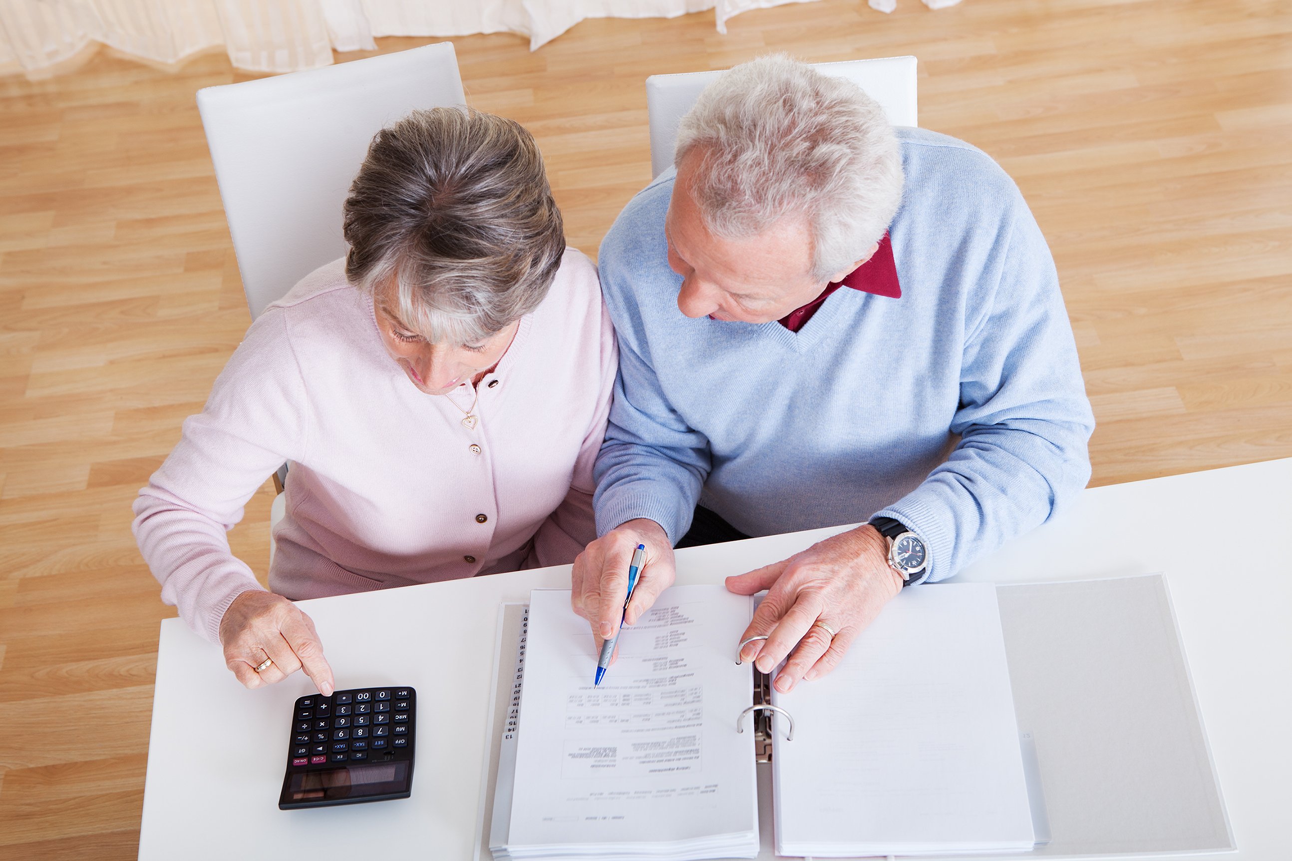 An older couple is shown from above, sitting at a desk and studying numbers.