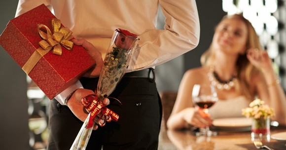 Someone holding a rose and a gift approaching a date.