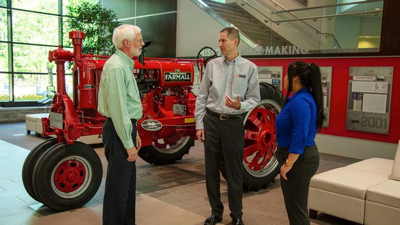Three people next to a red tractor.