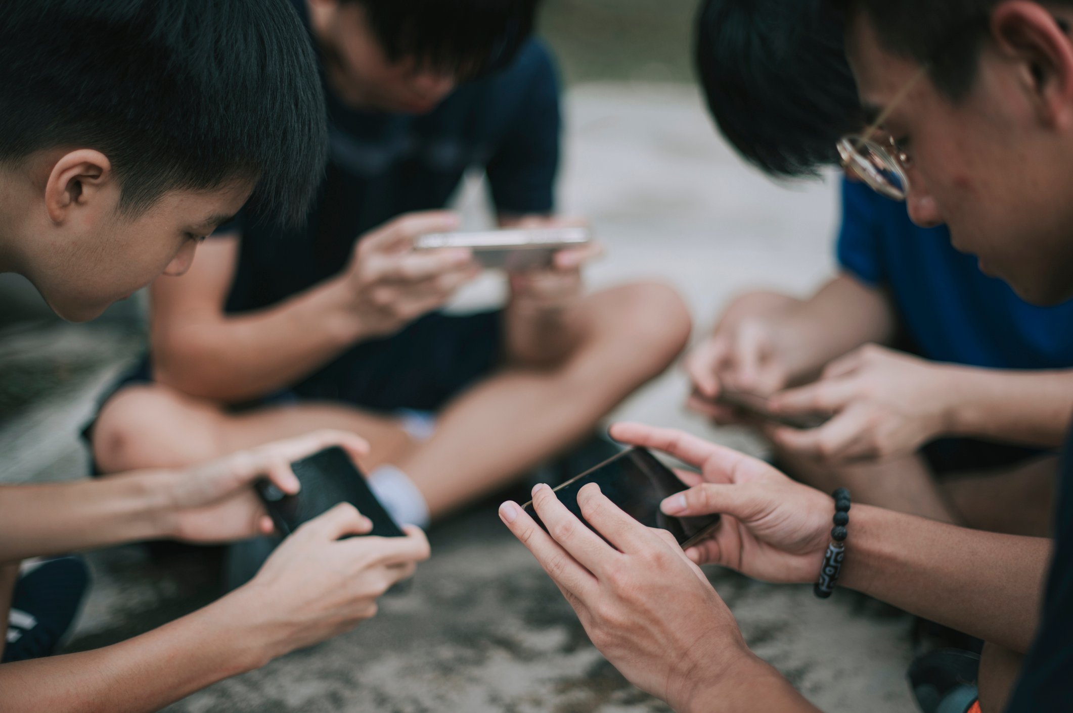 Four people sitting together looking at their smartphones.