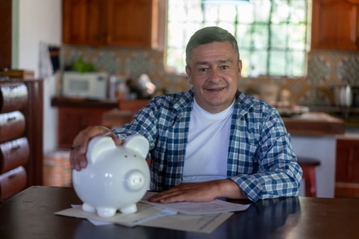 Someone is sitting at a kitchen table, with a piggy bank.