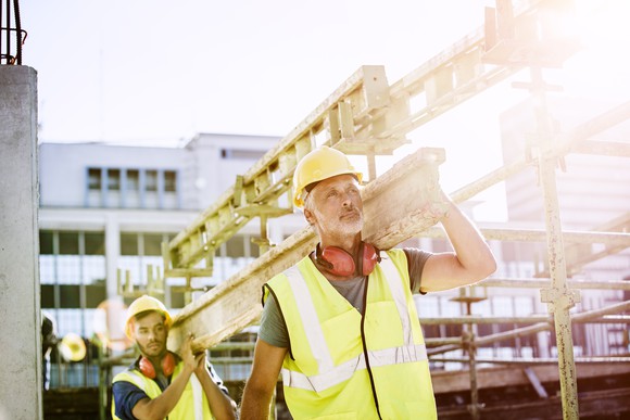 Two construction workers carrying a beam.
