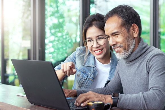 Two smiling people looking at a laptop.