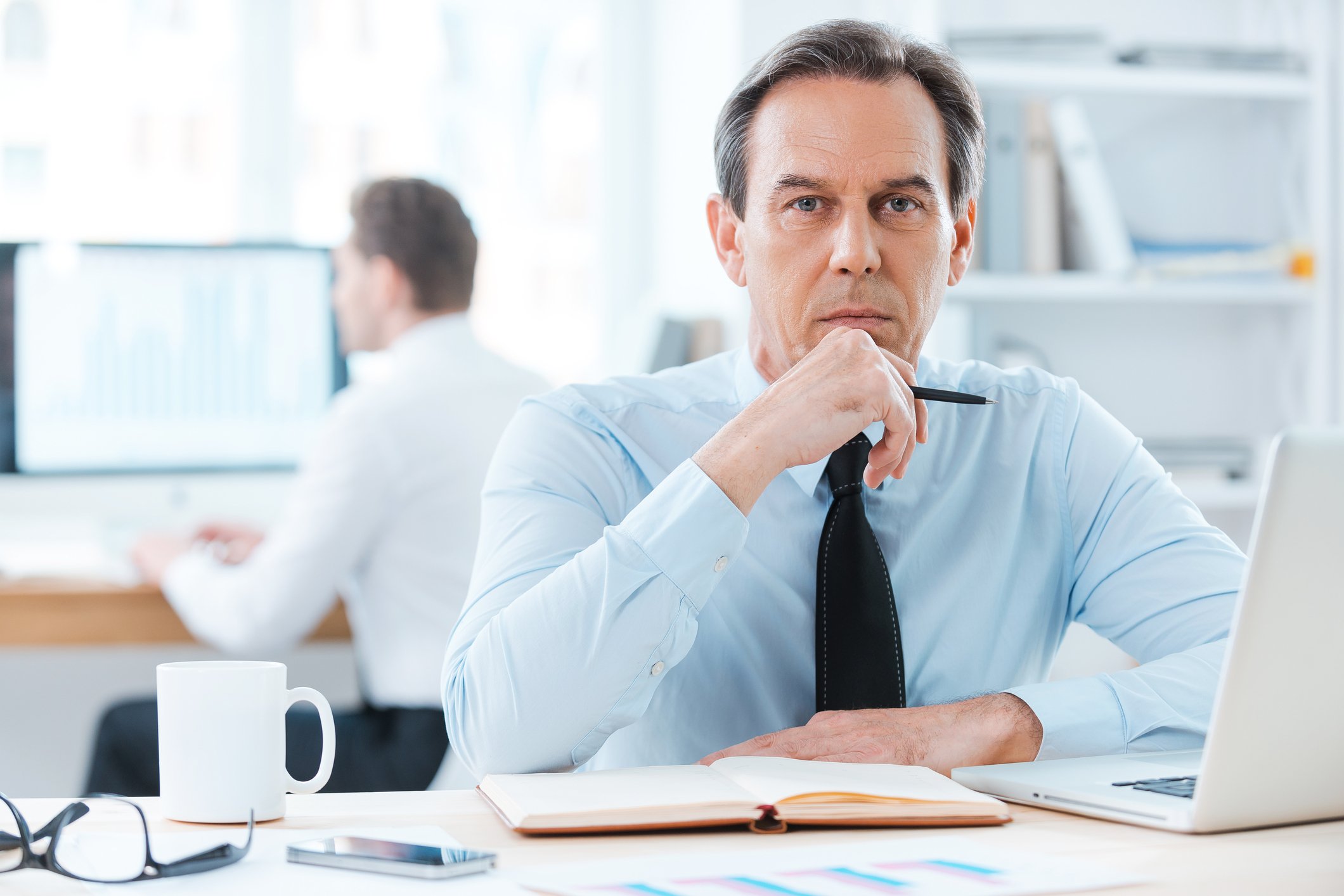 Businesspeople working at their desks in front of desktop computers or laptops. 
