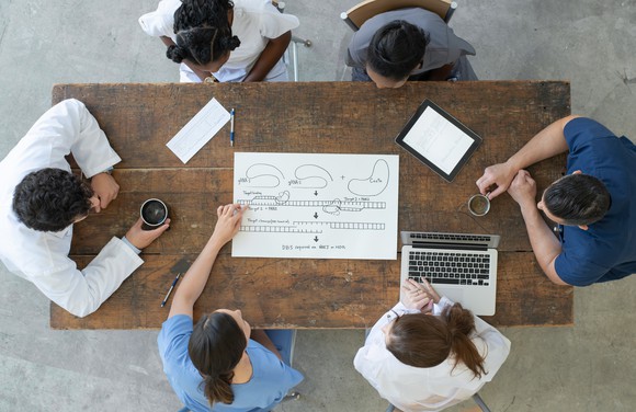 Six people gathered around a table collaborate on a project.