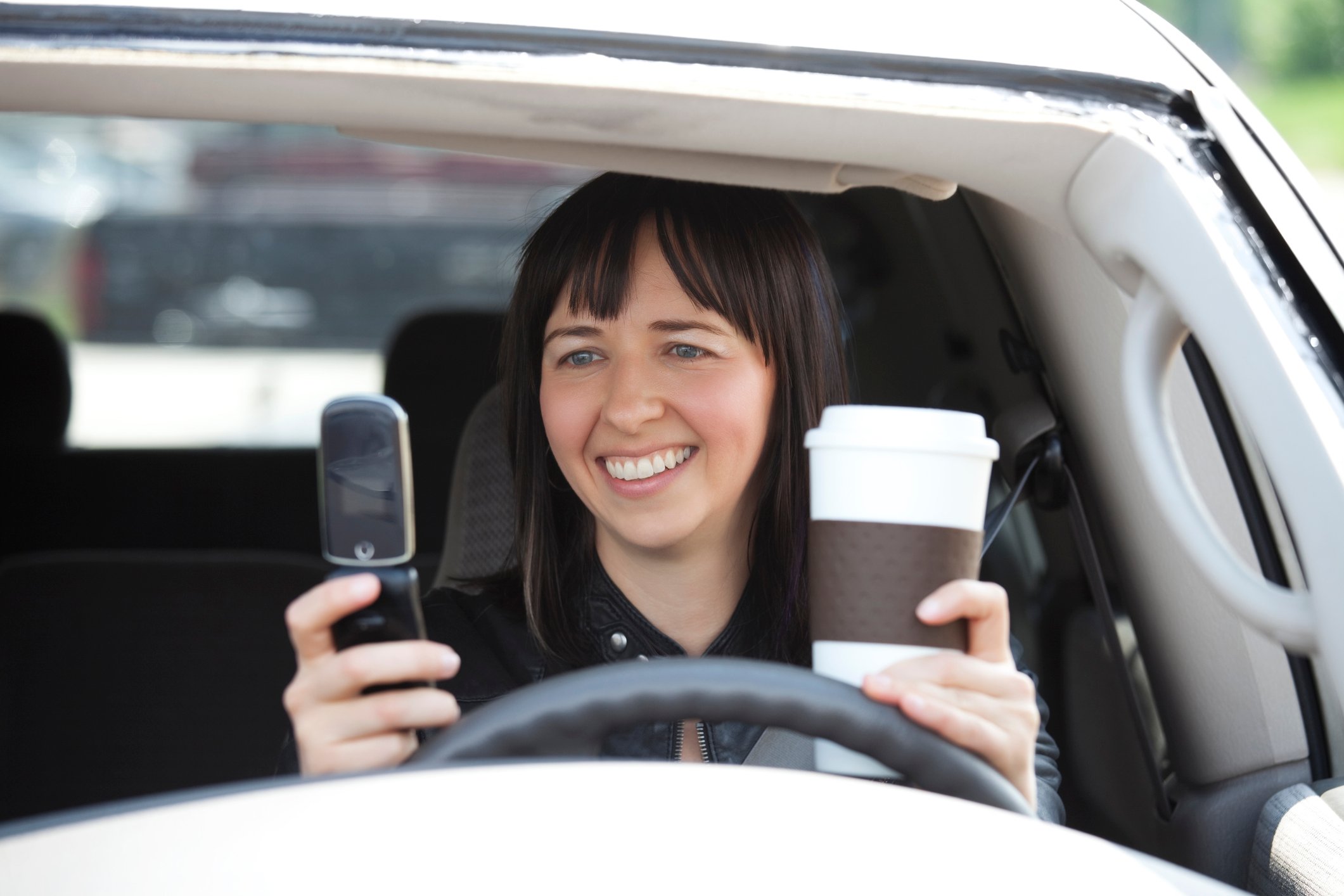 Person in car looking at phone and drinking coffee.