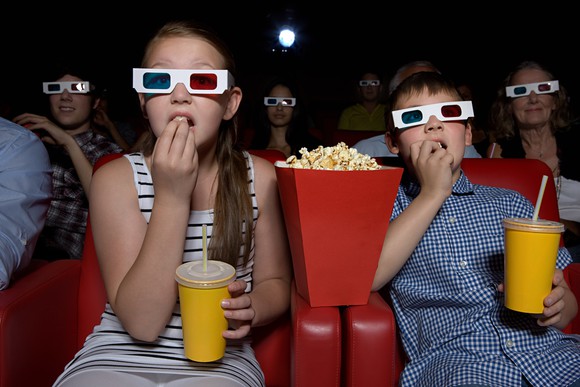 A group of people eating popcorn and watching a movie in a movie theater.