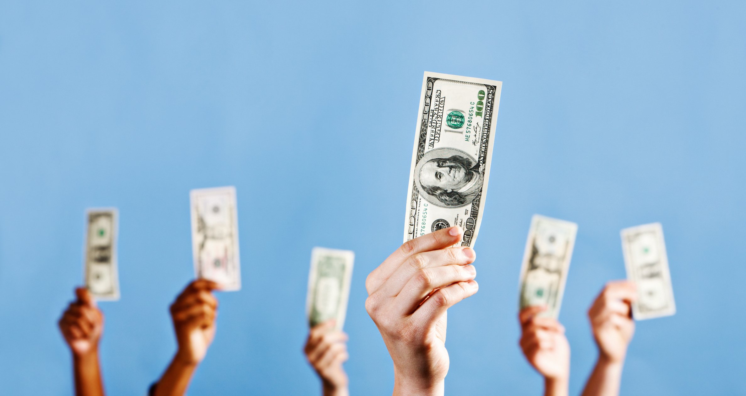 Hands holding U.S. currency in the air.