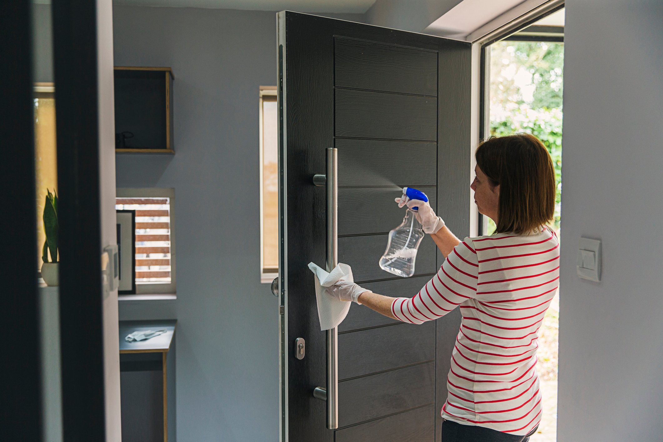 A person spraying cleaning product on a door handle.