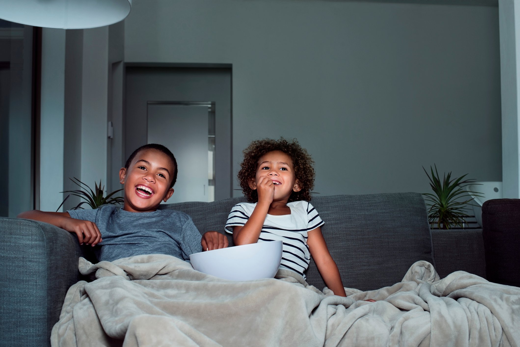 A boy and a girl watching  television and eating popcorn.