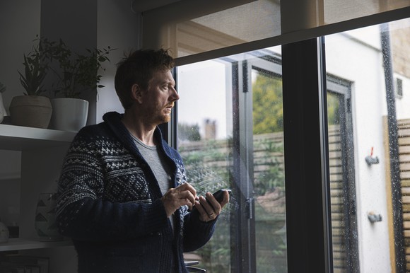 A man holding his phone, looking out the window.