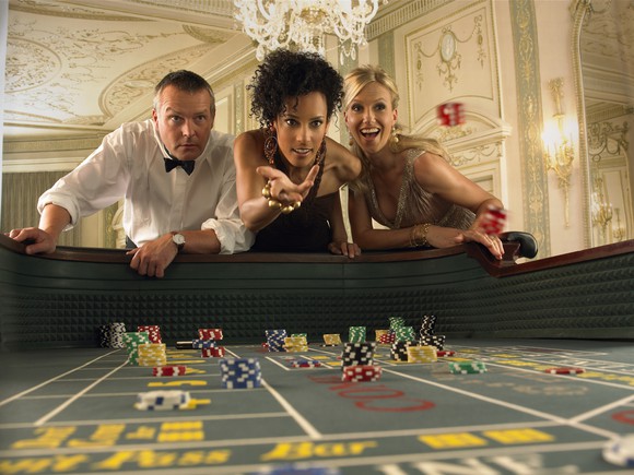A woman rolling dice during a casino craps game, with other people watching.
