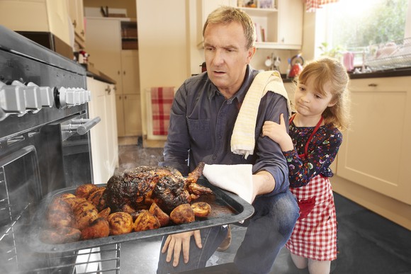 An adult and child pull a burned turkey out of the oven and look at it with dismay.