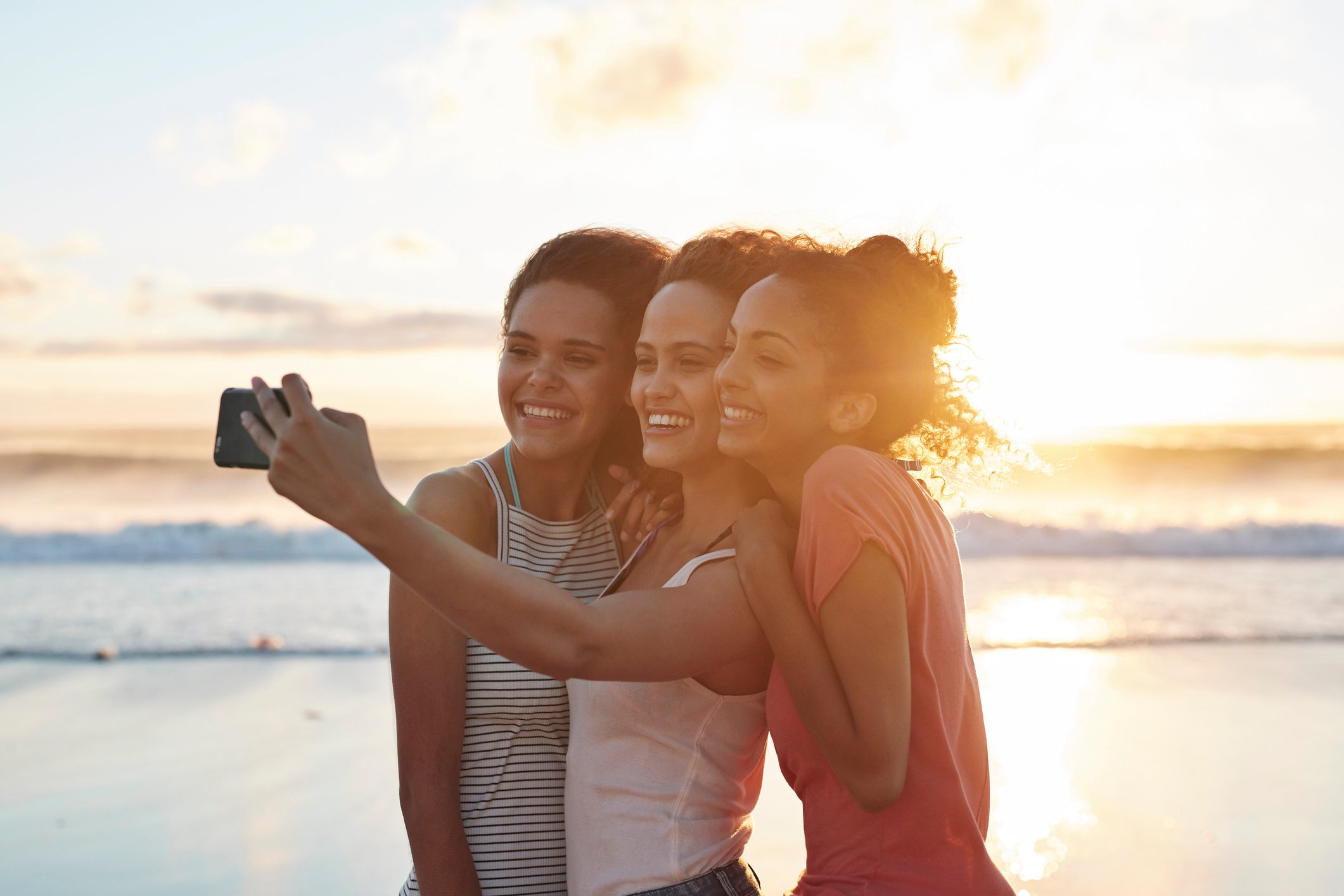 three people taking a selfie on the beach at sunset