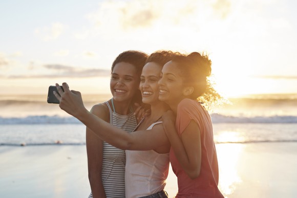 three people taking a selfie on the beach at sunset