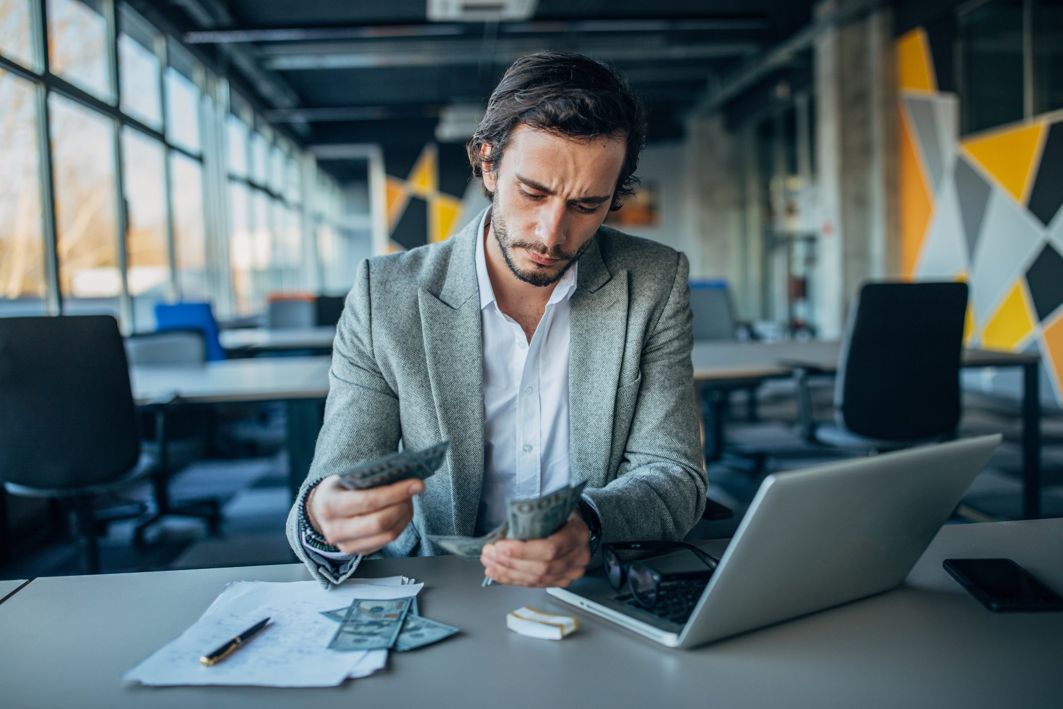 Young investor counting cash in front of a laptop.