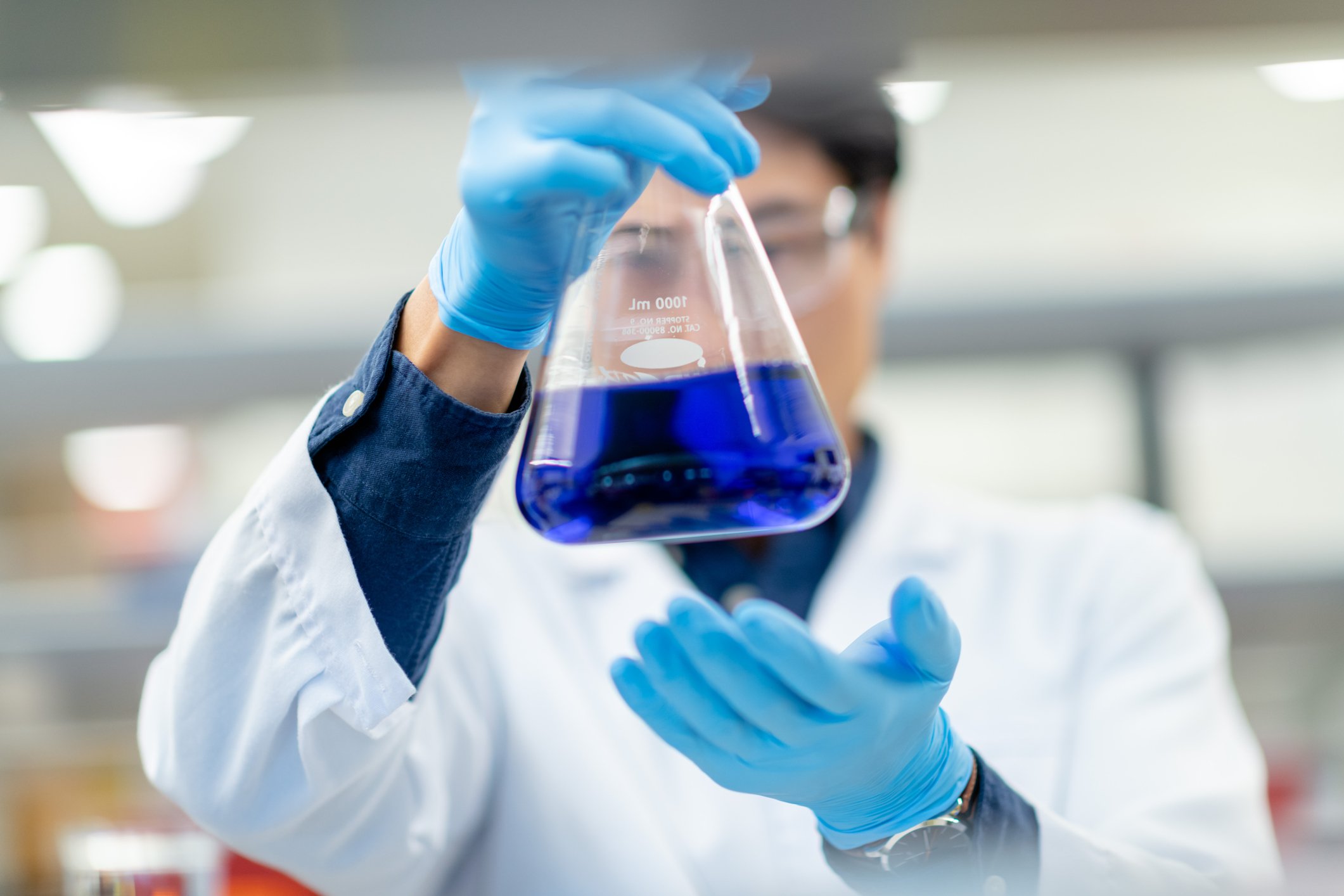 Laboratory worker looks at a blue chemical solution in a beaker.