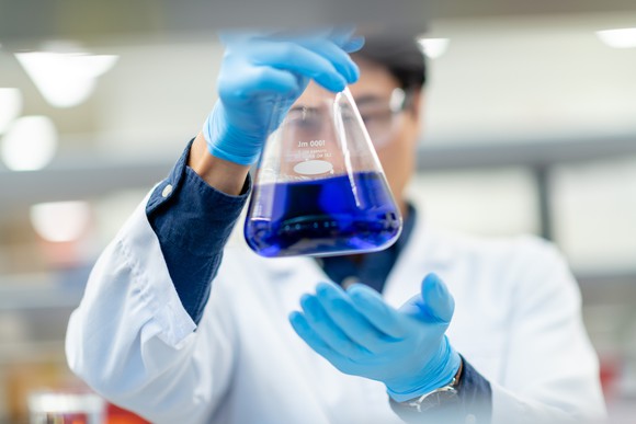 Laboratory worker looks at a blue chemical solution in a beaker.