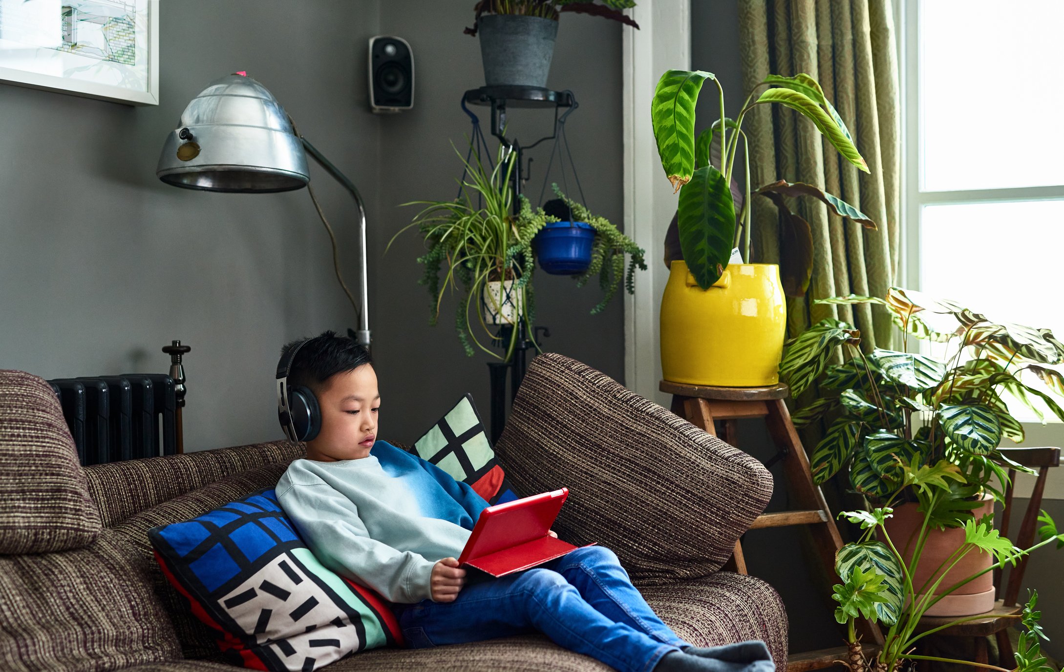 Child with headphones on couch playing games on tablet computer.