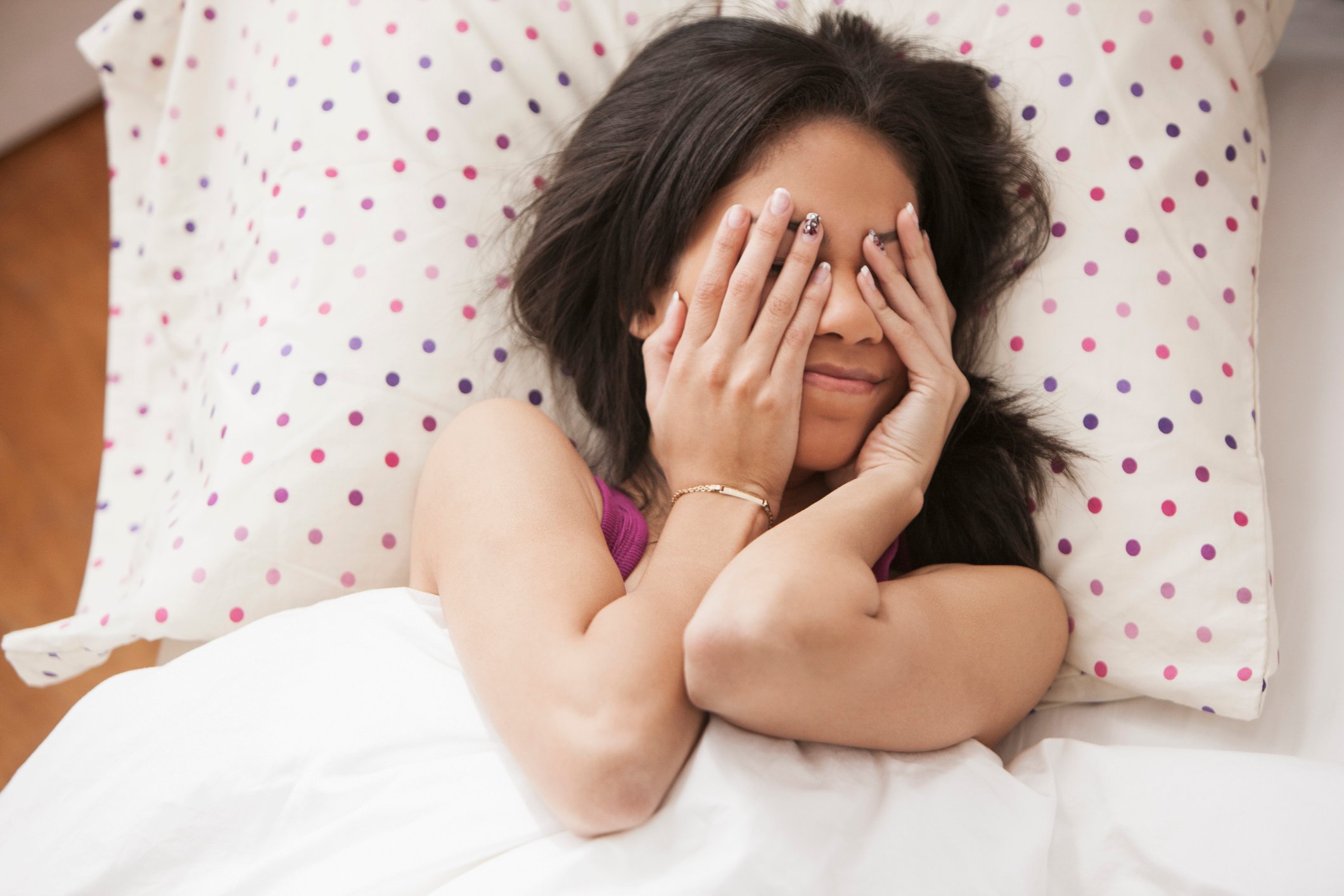 A person covers their eyes while lying down on a pillow.