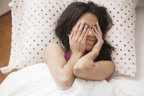 A person covers their eyes while lying down on a pillow.