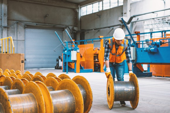 A worker rolls a giant spool designed for wiring.