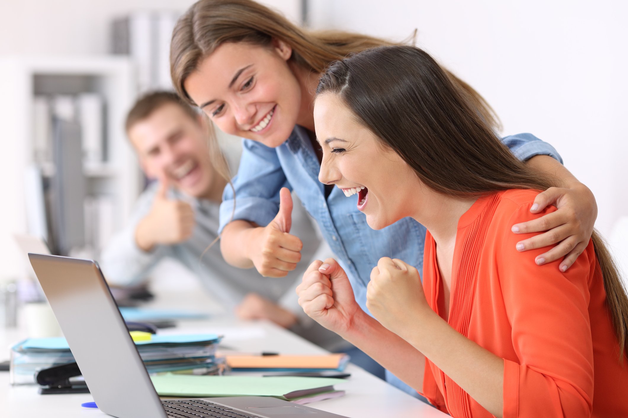 A team of office workers celebrate what they see on their laptop computers.