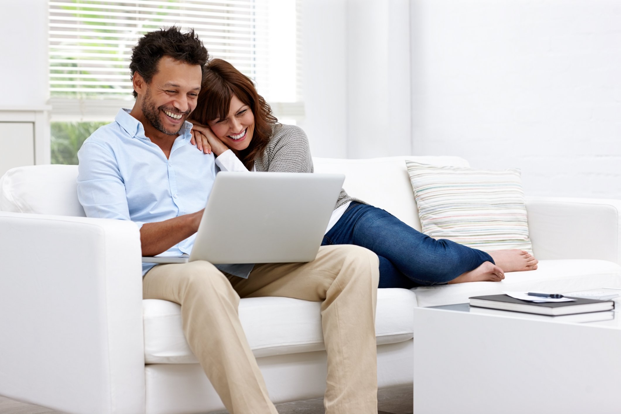 Two smiling people sitting on a sofa and looking at a laptop.