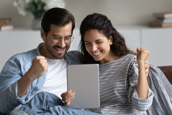 Two smiling people looking at a touchscreen tablet.