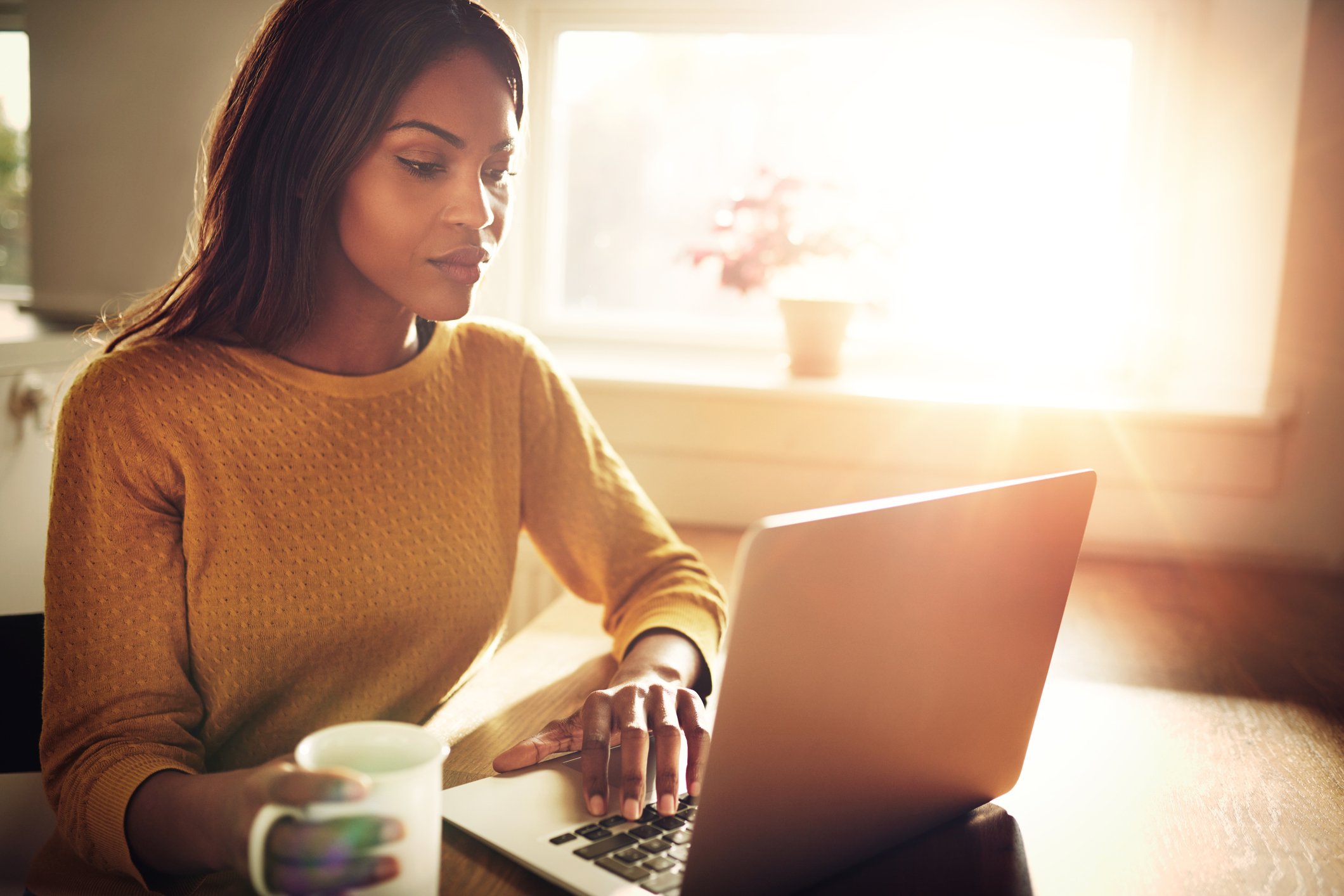 Adult looking at laptop and holding coffee cup.