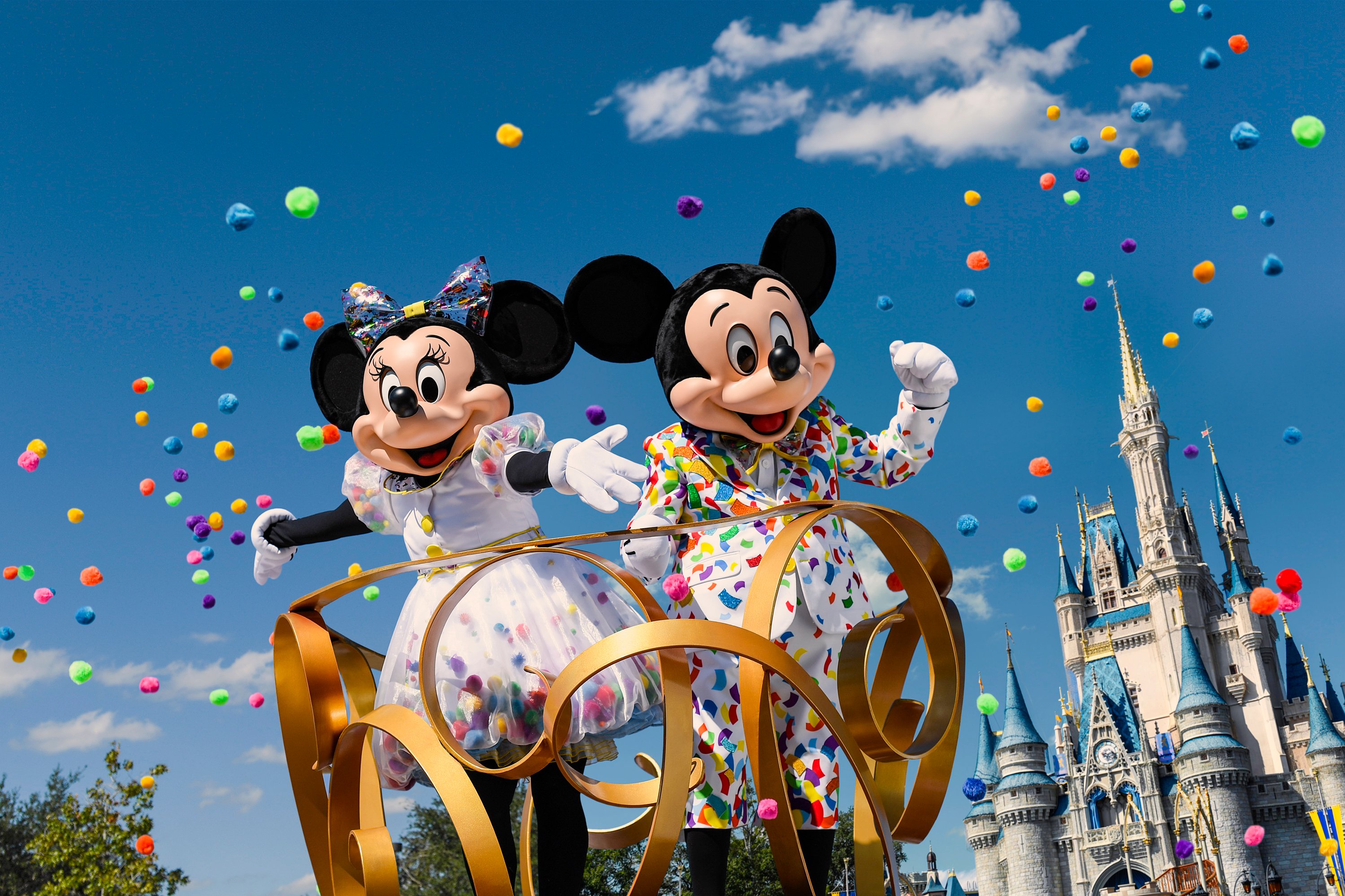 Mickey and Minnie in a parade with dozens of balloons released into the sky behind them.