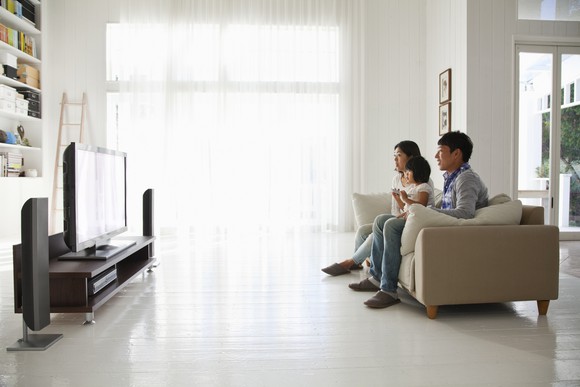 Three people watching TV in their living room while sitting on a couch.