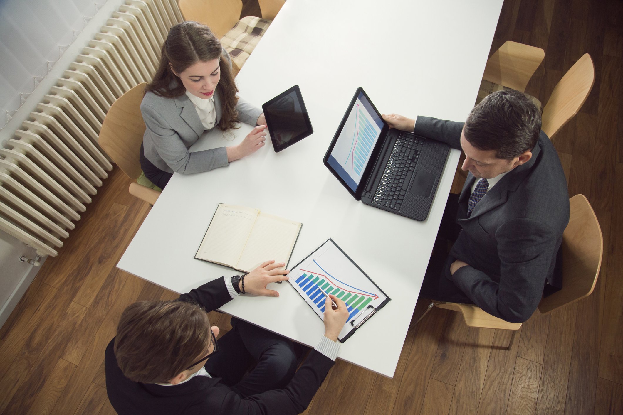 Three people looking at laptops and charts.