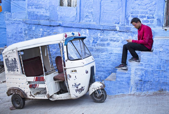 Person sitting and looking at their smartphone near a tuk-tuk taxi. 