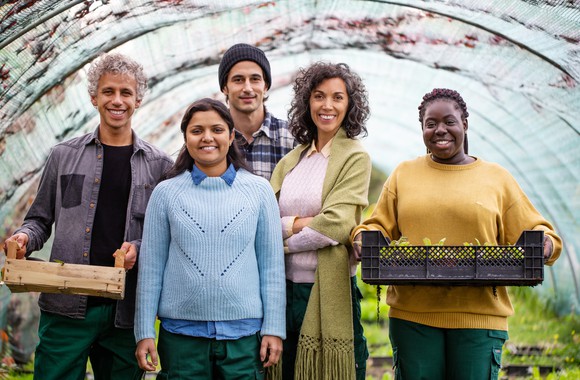 Coworkers in a greenhouse gather together while holding some of their products.