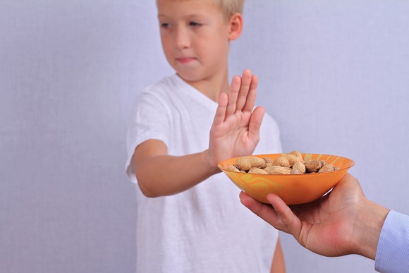 A child holding hand up to a bowl of peanuts.