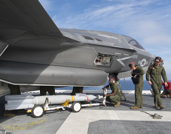 Navy personnel work on the deck of the aircraft carrier USS America near an F-35B fighter jet