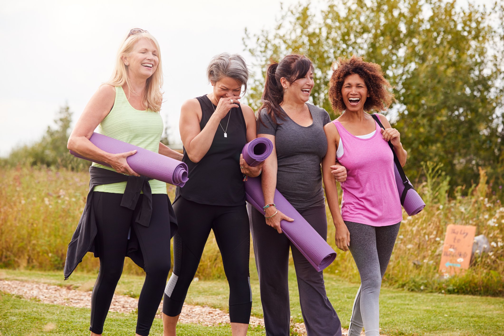 Four people walking outside together and carrying yoga mats.