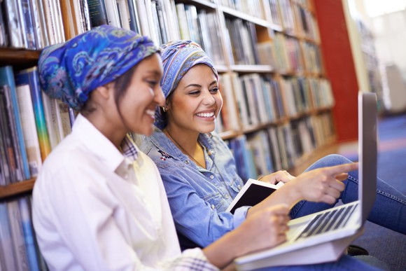 Friends sharing a laptop in a library.