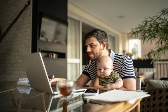 A person working at a computer with a baby in their lap. 