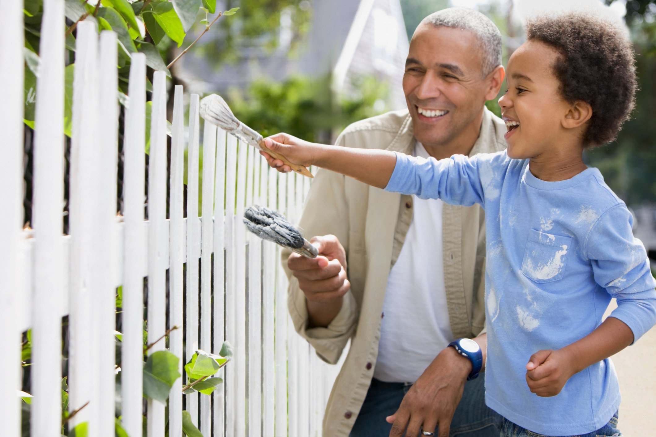 Two people painting a white picket fence. 