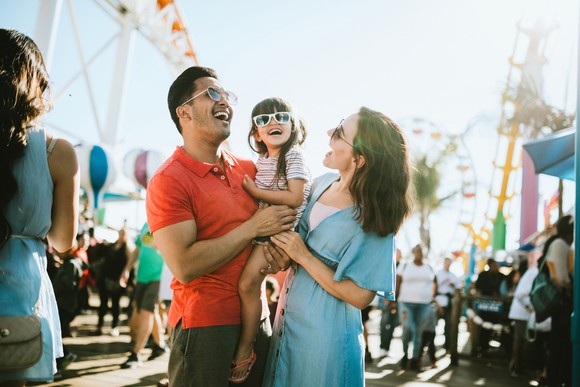 Two adults holding a child at a theme park. 
